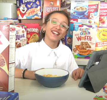 Fillette assise à un bureau entourée de boites de céréales diverses