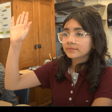 Une écolière en classe lève la main