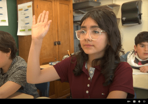 Une écolière en classe lève la main